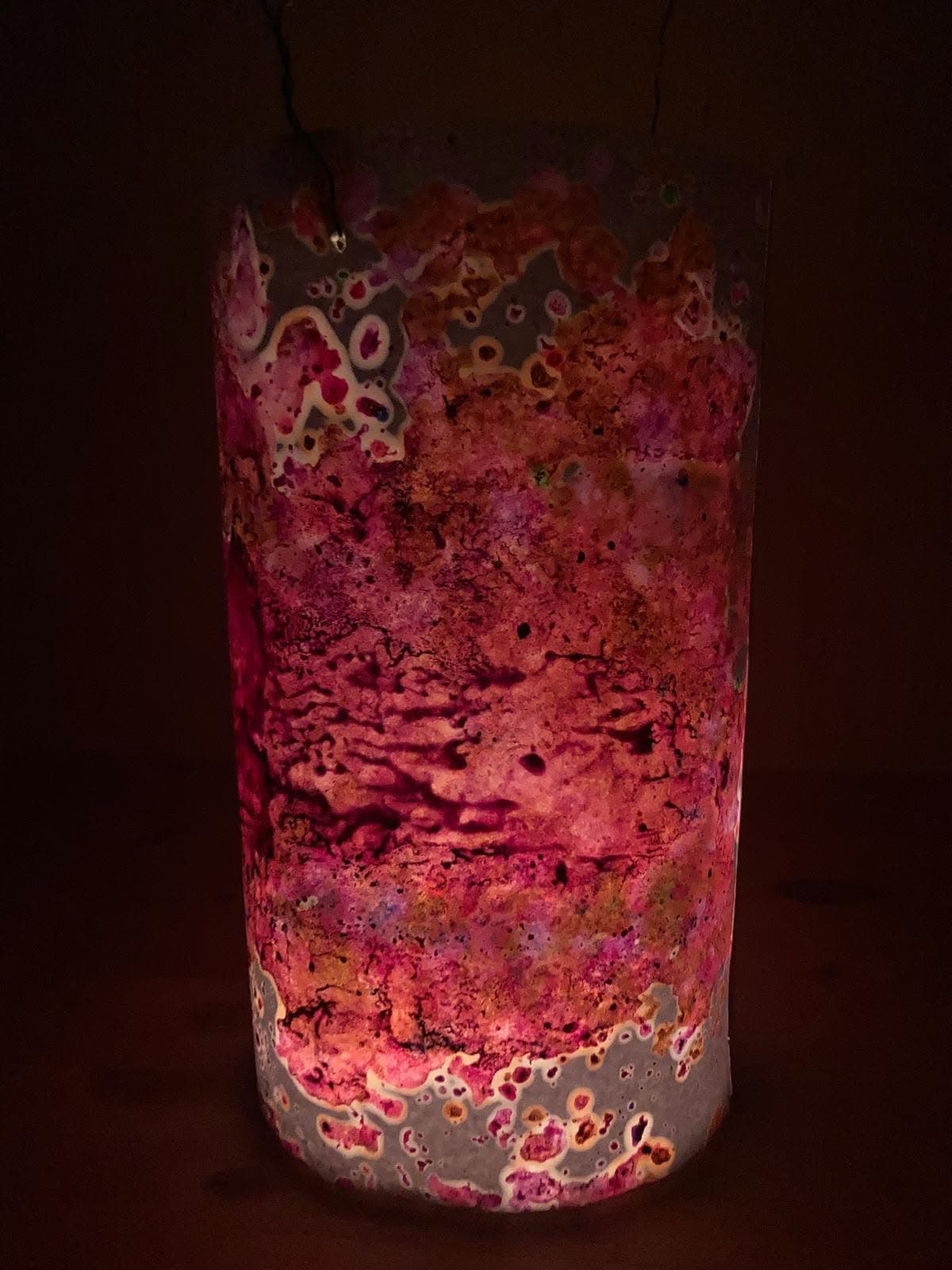 Rozsvícený ručně malovaný lampion s růžovo-oranžovými skvrnami ve tmě